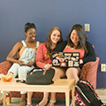 three seated students look at a laptop