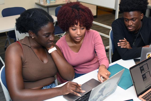 Three students doing homework around a table