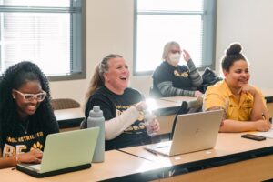 Four students in front of their laptops, smiling during a lecture